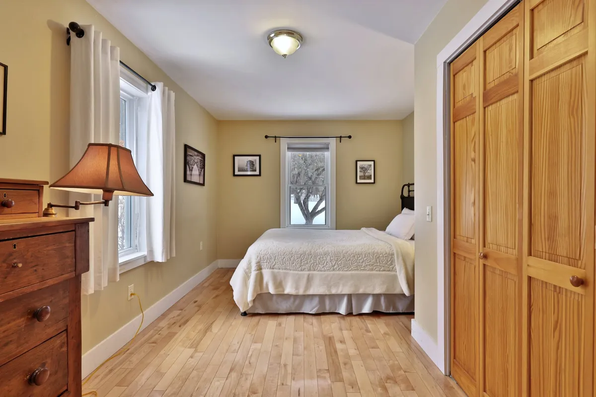 A tranquil bedroom featuring white bedding, a wooden dresser, and a window letting in natural light. The uncluttered space feels airy, peaceful, and ideal for restful sleep, matching the narrative focus on serene retreats and comfortable arrangements.