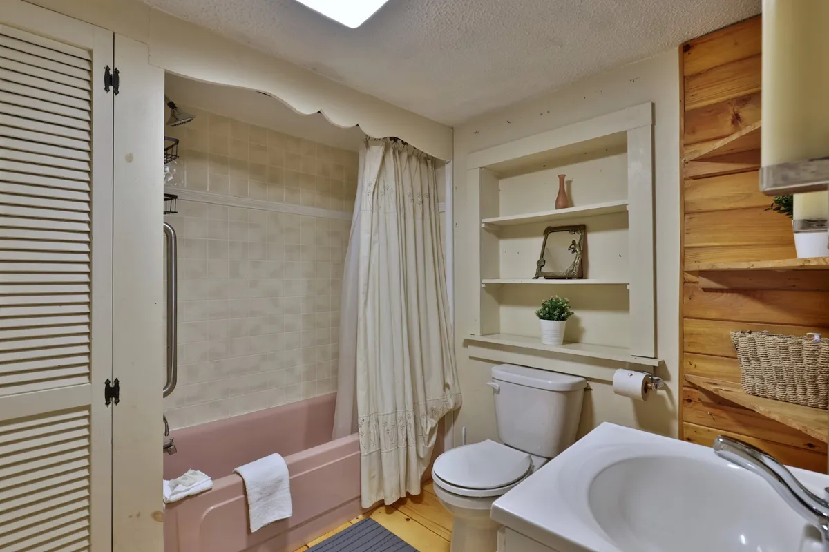 A well-appointed bathroom with a bathtub, shelves, toilet, and sink. The layout is practical and inviting, with subtle decor that suggests modern fixtures and a focus on relaxation and rejuvenation after an active day.