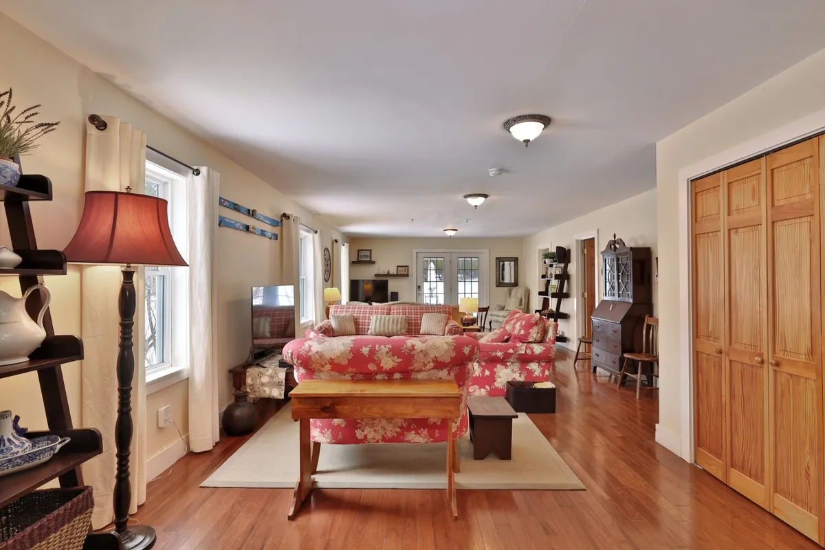 A living room scene featuring a floral patterned sofa, wooden coffee table, lamps with warm light, and bookshelves. The space is arranged for both socializing and relaxation, with plenty of room for families to gather, play games, or relax together.