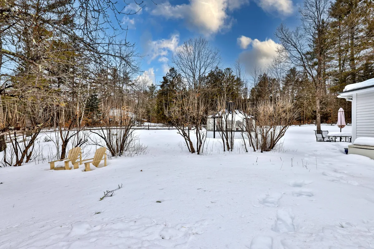 Adirondack chairs face a snowy yard with a charming gazebo in the distance, framed by tall trees. The peaceful scene evokes quiet moments sipping hot drinks, unwinding after a day outdoors, or gathering with friends for stargazing or storytelling.