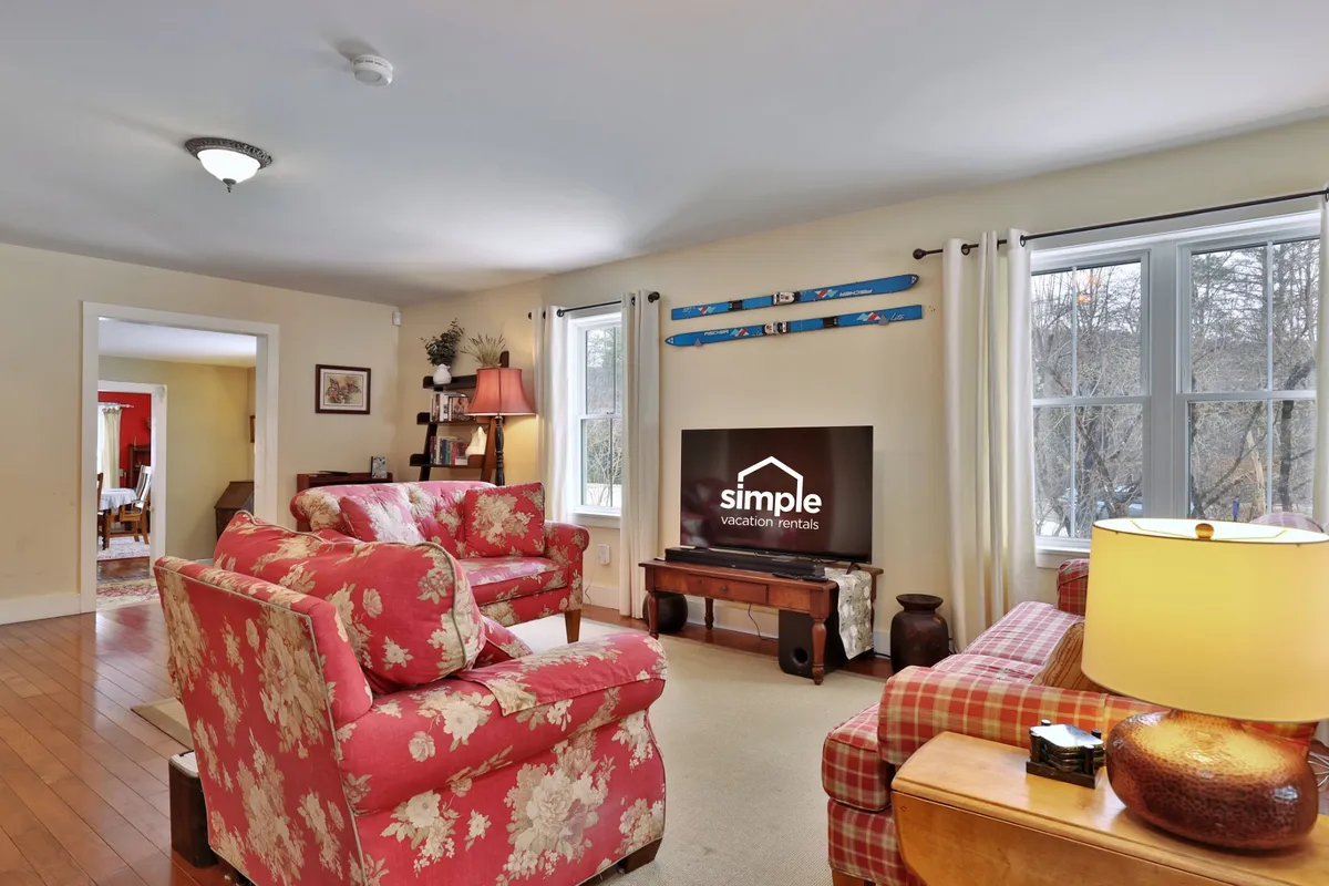 A comfortable living area featuring floral-patterned sofas, a central wooden coffee table, and a wall decorated with skis—subtly tying the interior space to the ski theme. The television set-up and inviting seating suggest warmth and relaxation after a day outdoors.