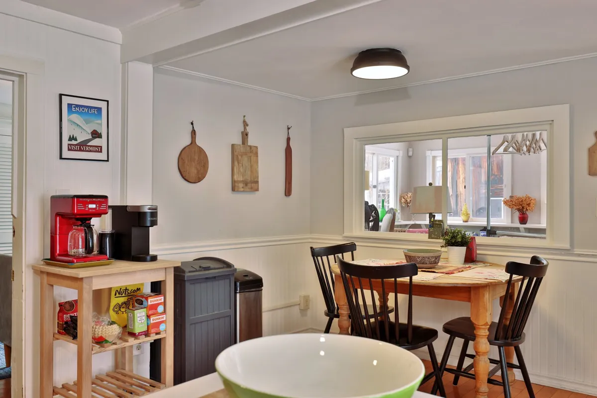 A cheerful breakfast nook with a kitchen table, coffee maker, decorative wall hangings, and a large window that fills the space with natural light. The atmosphere is perfect for quiet mornings or planning the day's adventures.