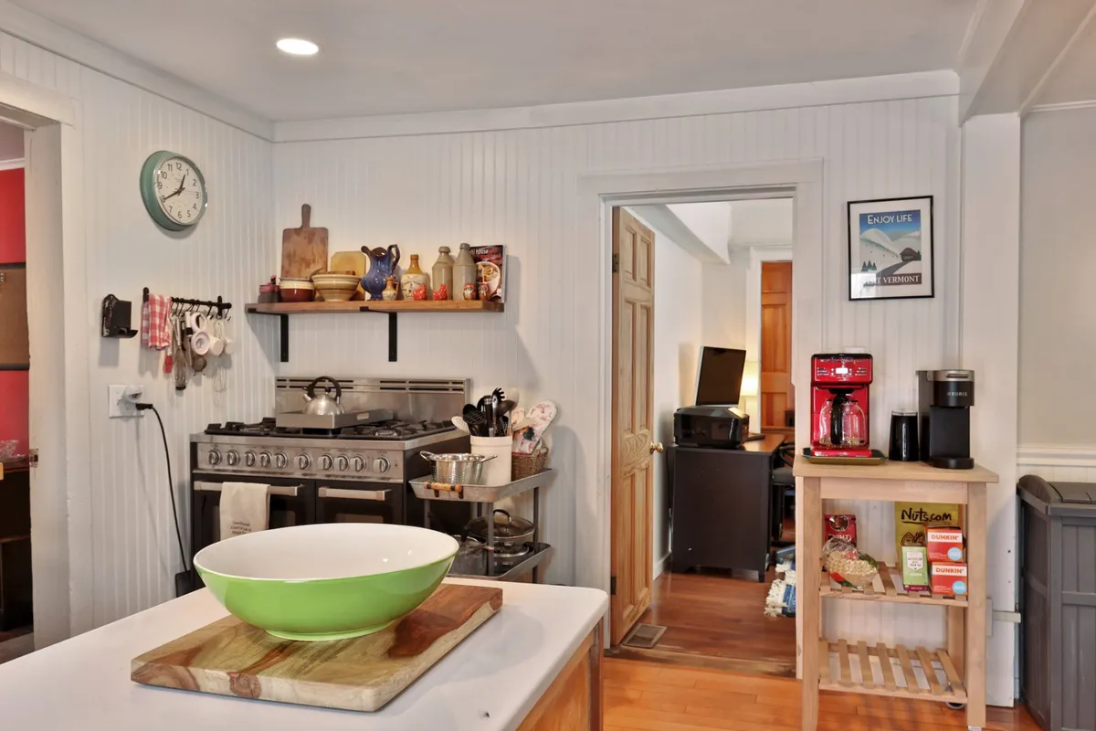 A modern kitchen scene with a stainless steel stove, a green bowl set on the island, and a variety of utensils ready for use. The space feels functional and warm, ideal for cooking and hosting.