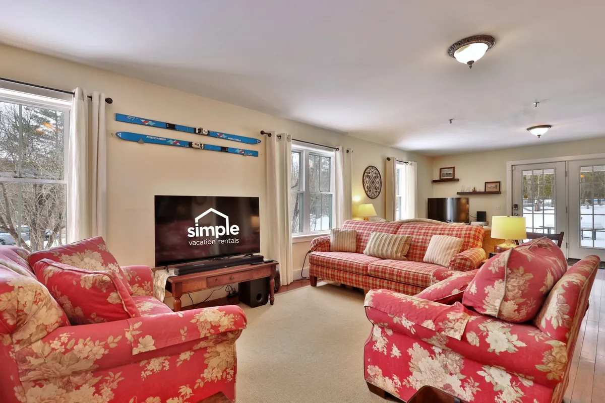 A cozy living room with colorful floral-patterned sofas, a television, large windows letting in natural light, and decorative vintage skis mounted on the wall, all arranged to create a welcoming atmosphere perfect for relaxing with family or friends.