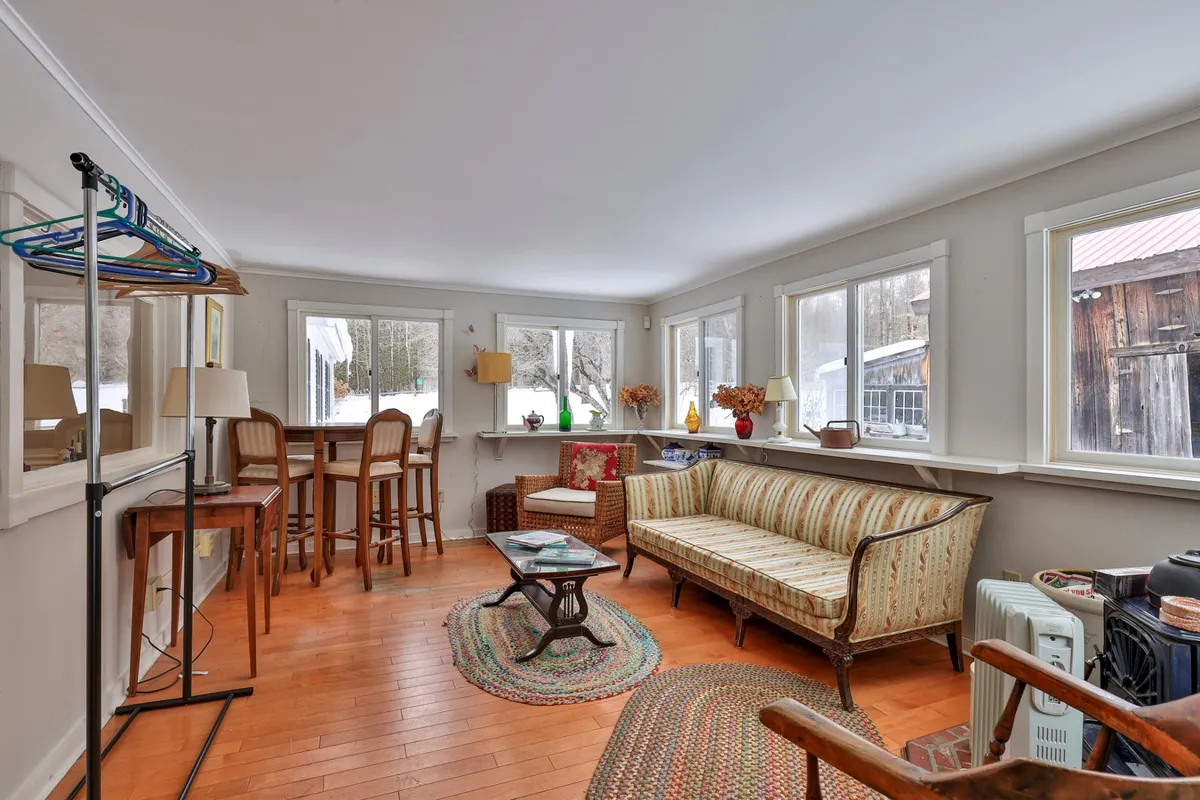 A sunlit living space featuring a striped sofa, wooden bar stools, large windows, and vibrant house plants. The room exudes a sense of relaxation and is set up for social interactions or quiet moments between festivities.