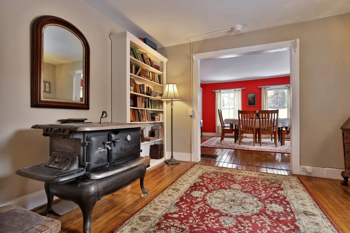 A warm dining area with a cast iron stove as its centerpiece, surrounded by a bookshelf and a dining table set for a group. The red walls and ambient lighting create an inviting, celebratory atmosphere perfect for gatherings.