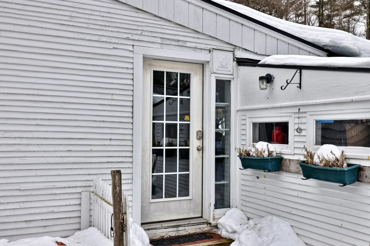 A warmly inviting entrance to the farmhouse, framed by snow-covered steps and planters, with the front door providing a cheerful welcome home after a day outside.